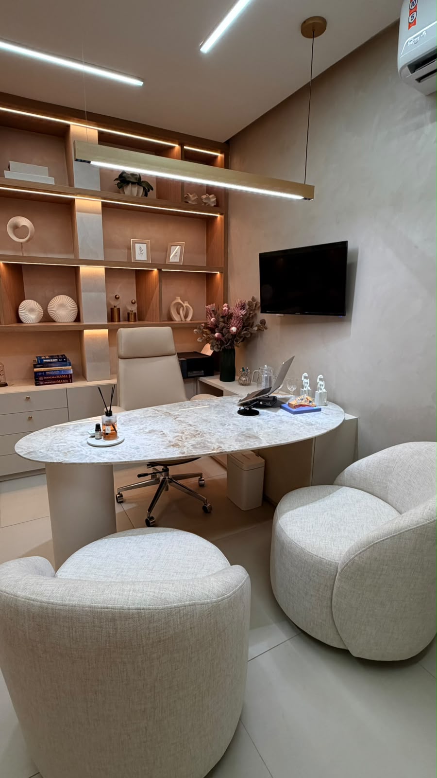 Consultório com mesa oval de mármore e estante iluminada