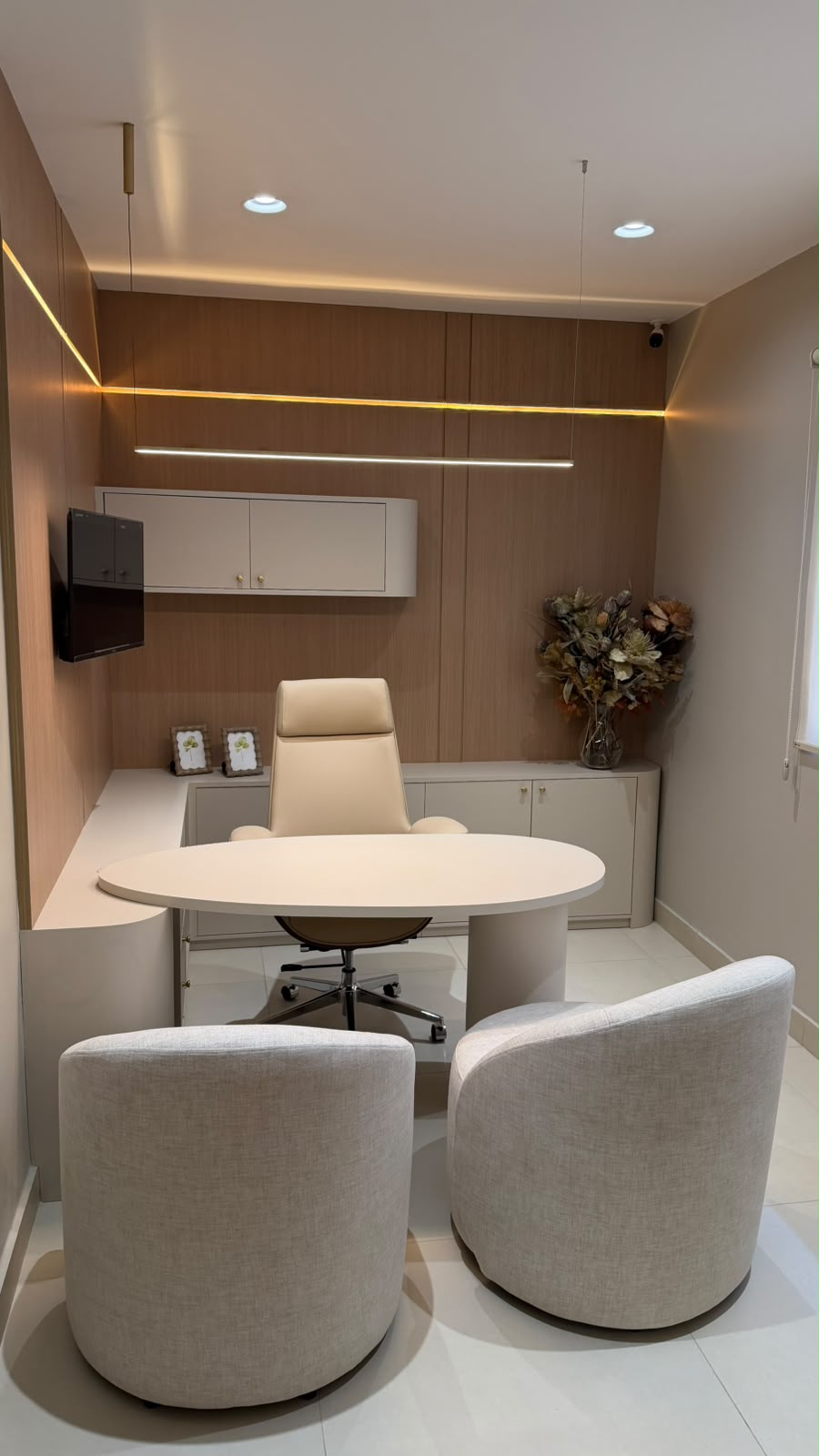 Consultório com mesa oval clara, poltronas e marcenaria amadeirada